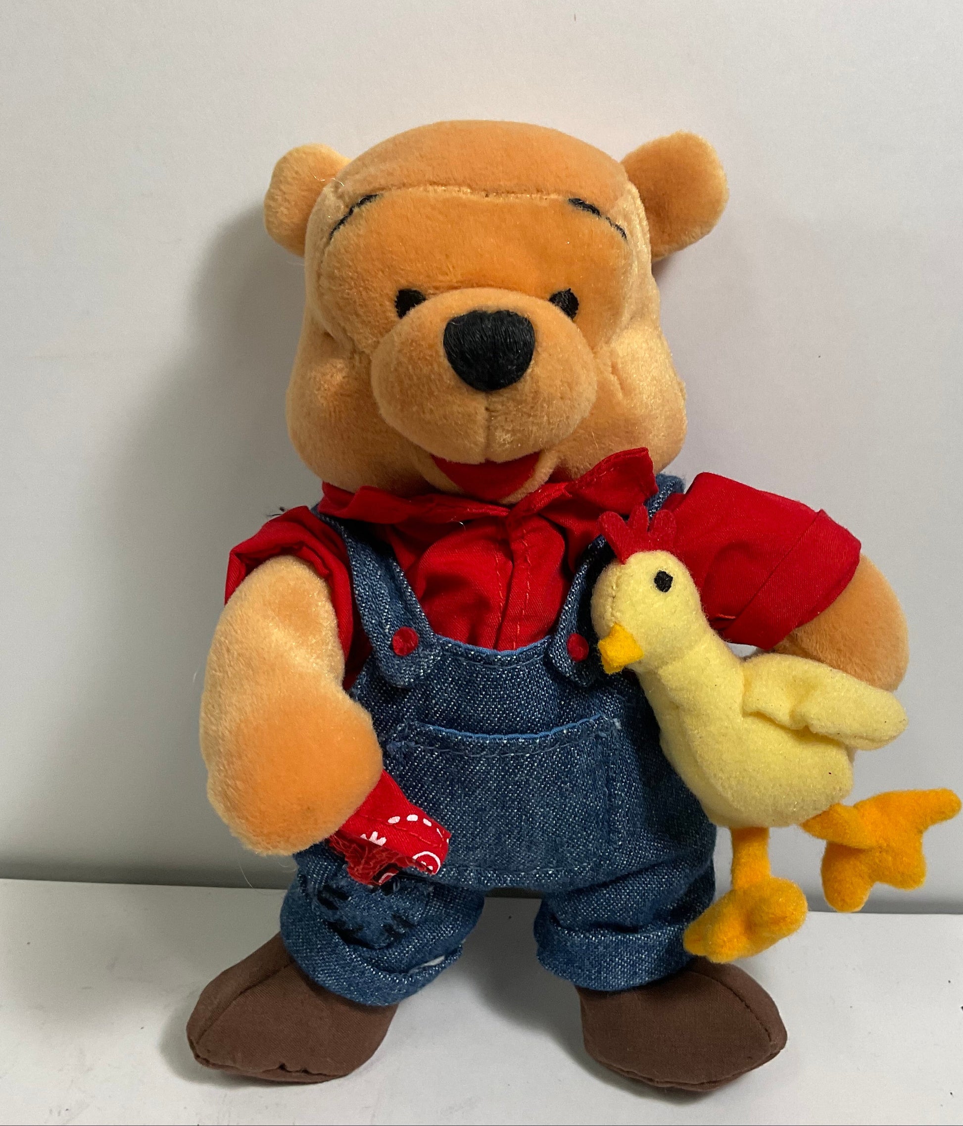 Plush toy of a bear in overalls with a duck on a white background